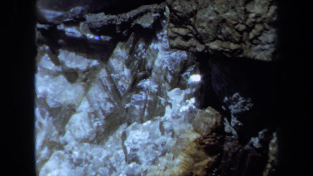Maine 8mm frame showing a rocky area near a house exterior, with dark film-edge or shadowed framing.