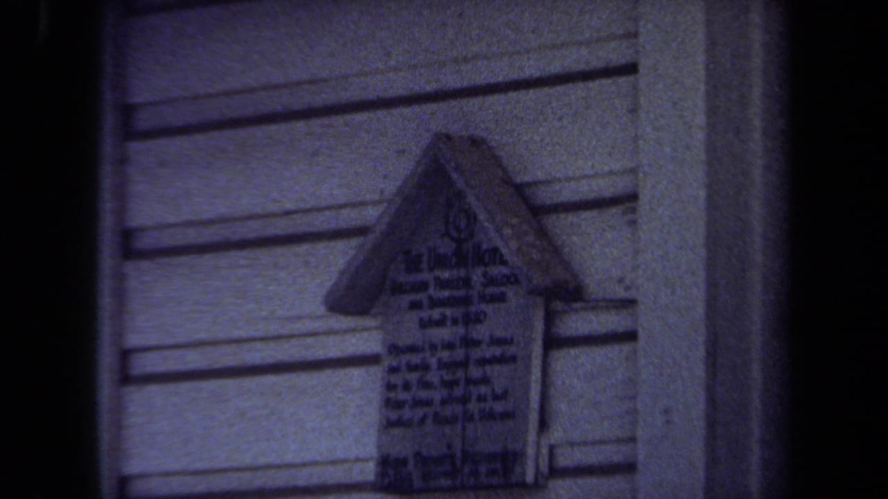 1971 Maine 8mm frame centered on a small house-shaped wooden marker with dark handwritten text on a clapboard wall.
