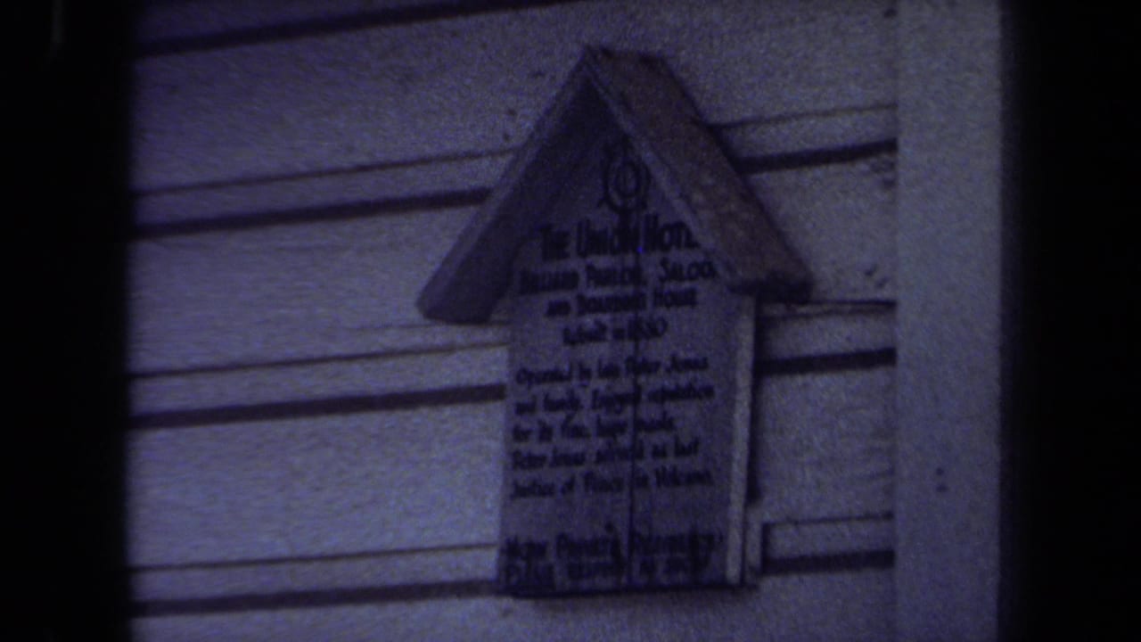 Small mounted sign on exterior siding, seen in dark handheld 8mm footage.