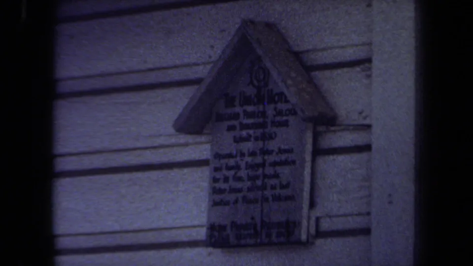 A small sign mounted on horizontal siding appears in a dark 1971 Maine 8mm frame, with text mostly unreadable.