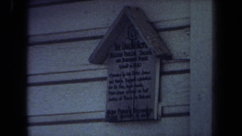 The 8mm frame shows a small sign fixed to exterior siding in Maine, with only partial lettering visible.