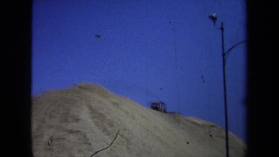 A broad sandy mound fills the frame, with a small vehicle and utility pole visible against the sky.