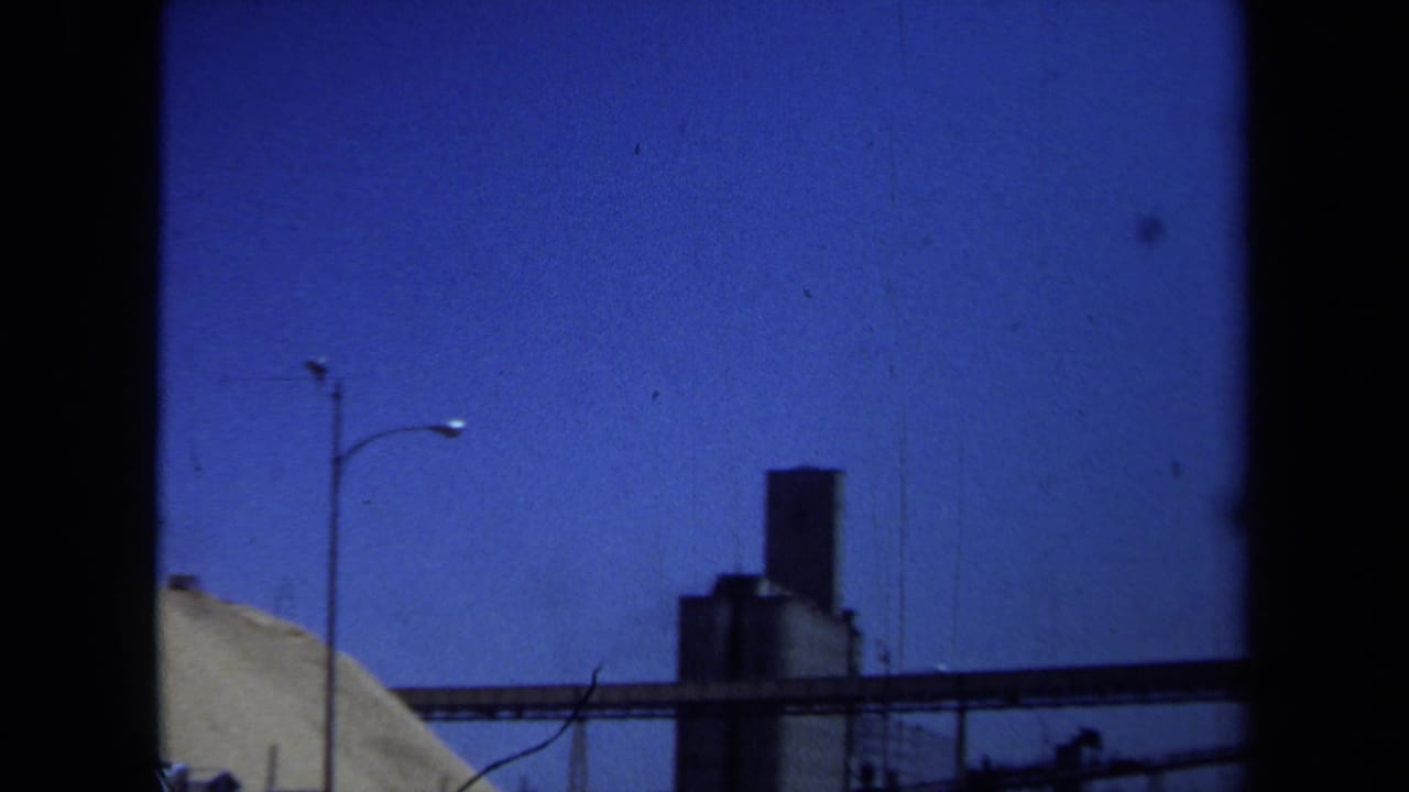 Industrial silo and conveyor belt beside a large material pile under open sky.