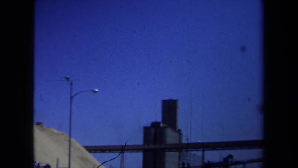 1971 Maine 8mm frame with a tall silo, conveyor structure, utility pole, and edge of a sand or gravel pile in an industrial yard.