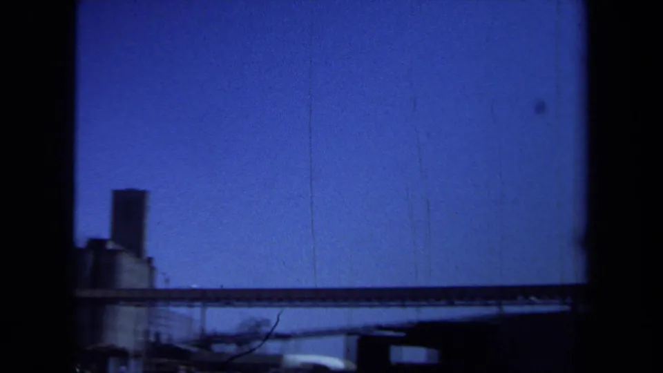 1971 Maine 8mm frame showing a silo, long conveyor, low industrial buildings, and a dark foreground edge from the film frame or obstruction.
