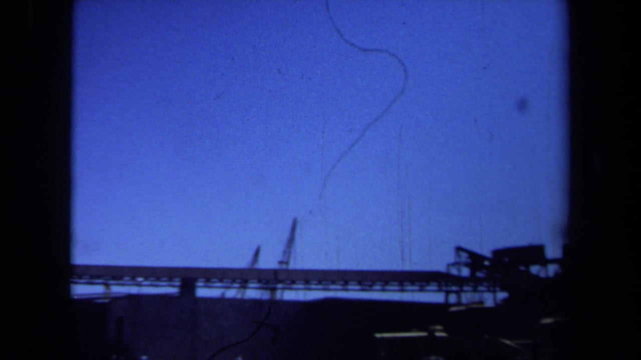Maine 1971 8mm frame showing silhouetted industrial construction equipment and a low structure against blue sky.