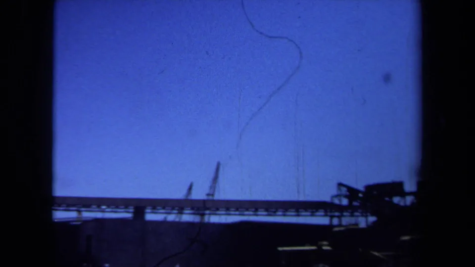 Maine 1971 8mm frame showing silhouetted industrial construction equipment and a low structure against blue sky.