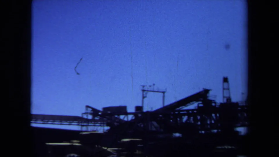 Maine 1971 8mm frame with a dark conveyor-like construction structure, crane forms, and machinery silhouetted at the horizon.
