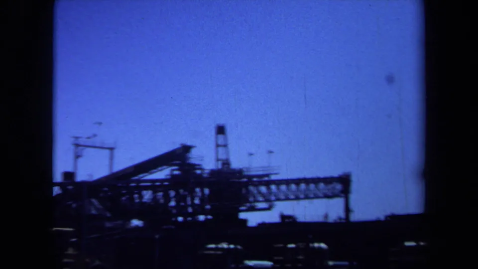 Maine 1971 8mm frame showing a large industrial truss or conveyor, vehicle silhouettes, and a narrow tower at the work site.