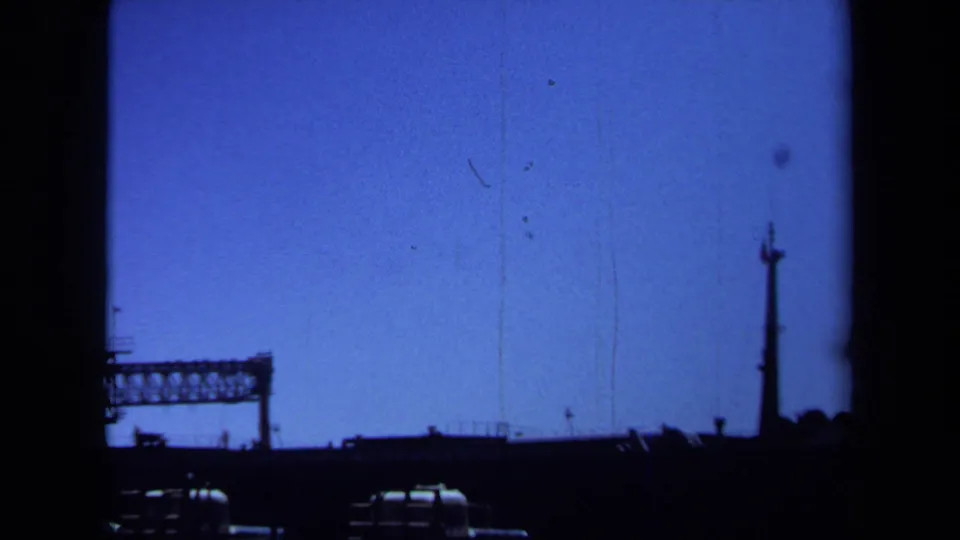 1971 Maine 8mm frame showing a far-off steel bridge or industrial span in silhouette beneath a blue sky.