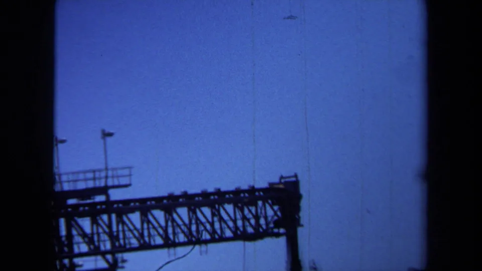 A silhouetted steel bridge span crosses the lower frame, with railings and poles visible against the blue sky.
