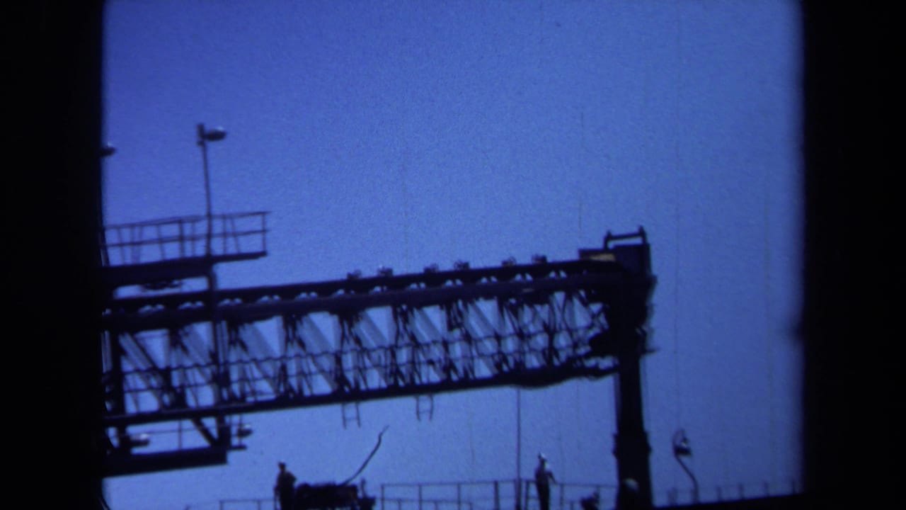 1971 Maine 8mm frame showing a dark overhead gantry or sign structure silhouetted against bright blue sky.