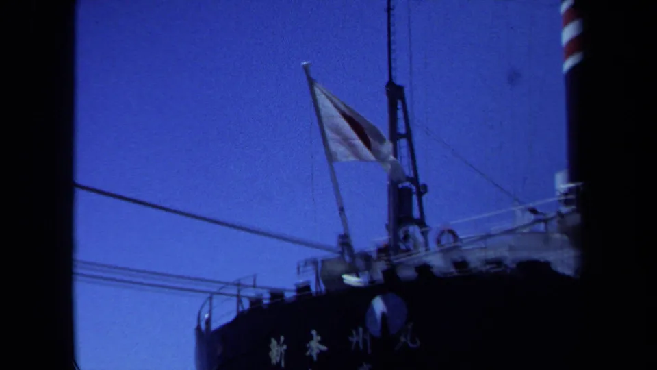 1971 Maine home-movie frame pulling back to show the Japanese flag above the ship deck and a striped smokestack.