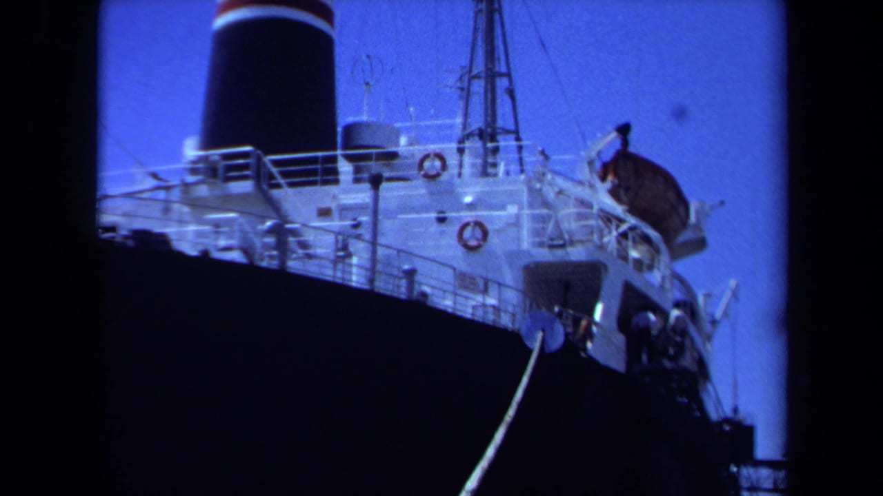 1971 Maine 8mm frame showing a large moored ship from below, with dark hull, white superstructure, black banded smokestack, and rope line.