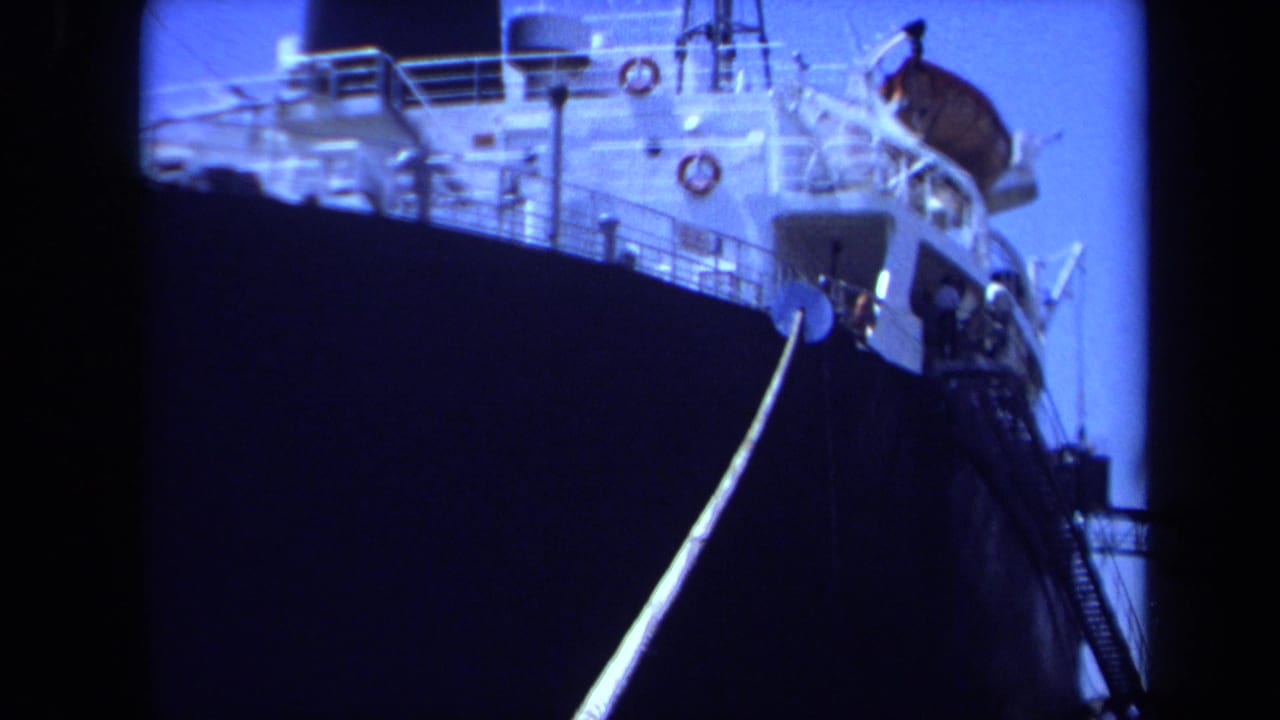 1971 Maine home-movie frame of the ship's bow and white upper deck, with a taut mooring line leading down toward the pier.