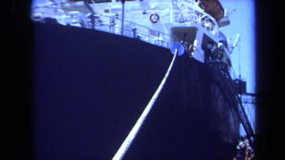 1971 Maine 8mm frame showing the vessel's bow sliding past the camera, with the mooring line prominent against the dark hull.