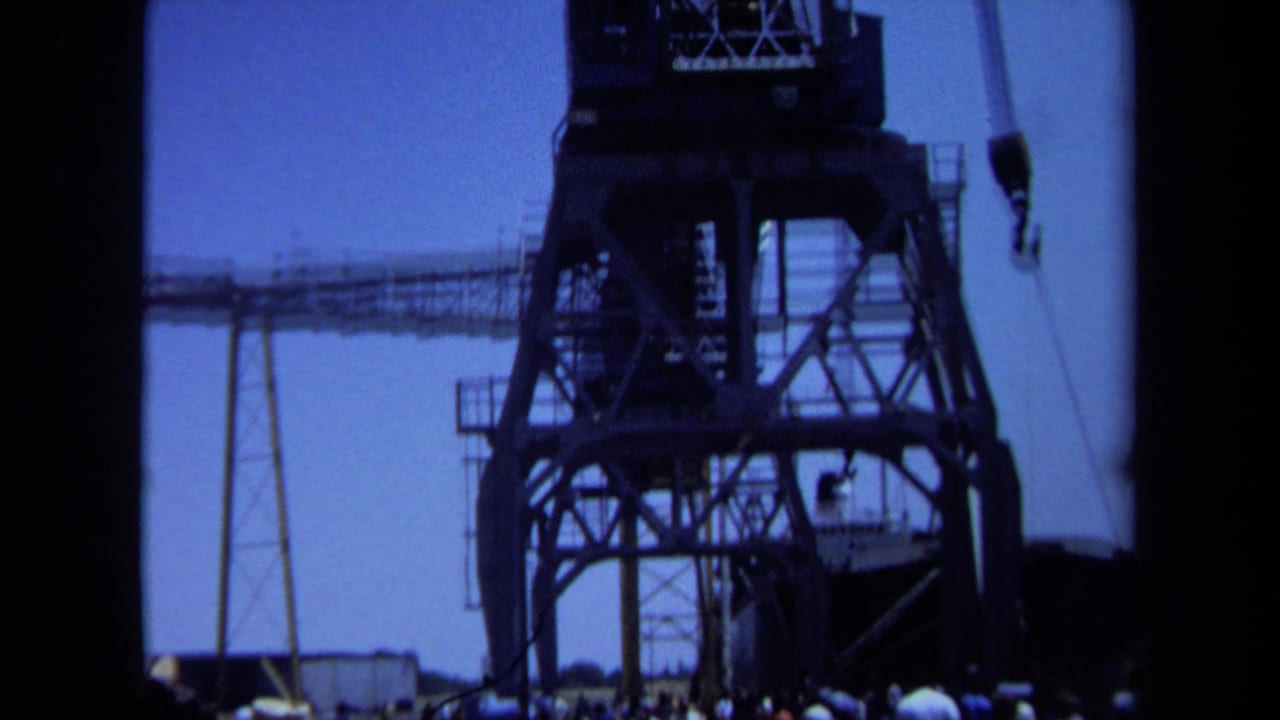 1971 Maine port view with the crane tower, suspended hook, and distant crowd visible below.