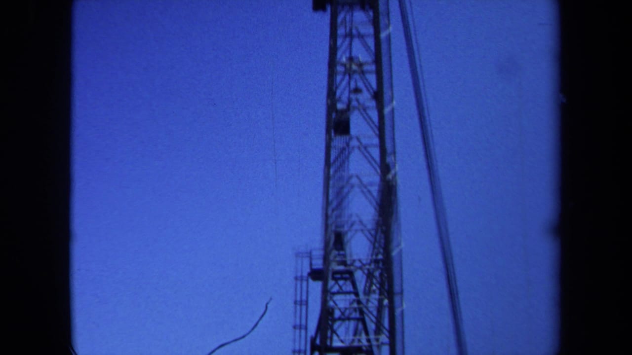 1971 Maine 8mm frame showing part of a tall lattice crane or metal tower silhouetted against a saturated blue sky.