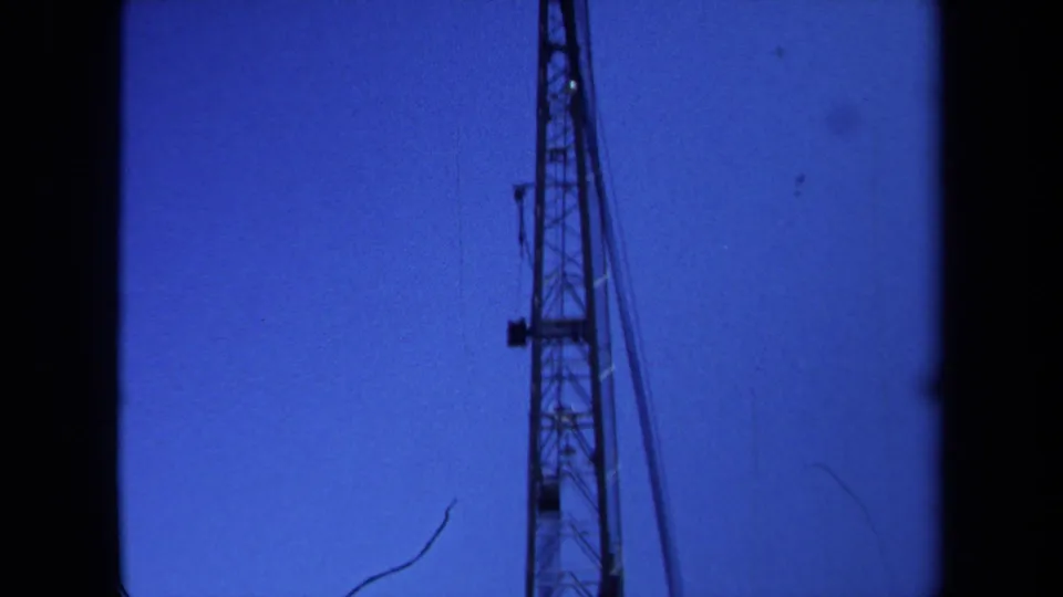 1971 Maine 8mm frame with the upper portion of a crane or metal tower and its cables seen against a clear blue sky.