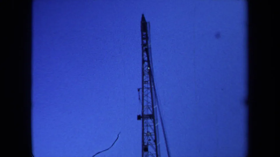 1971 Maine 8mm frame showing a tall narrow crane or tower section framed low against a blue sky with home-movie borders.