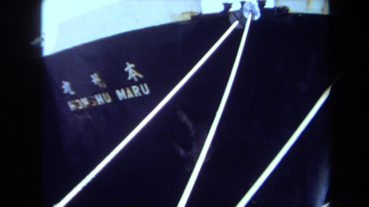The dark bow of the KONSHU MARU shows Japanese characters, gold lettering, white deck structure, and taut mooring lines.