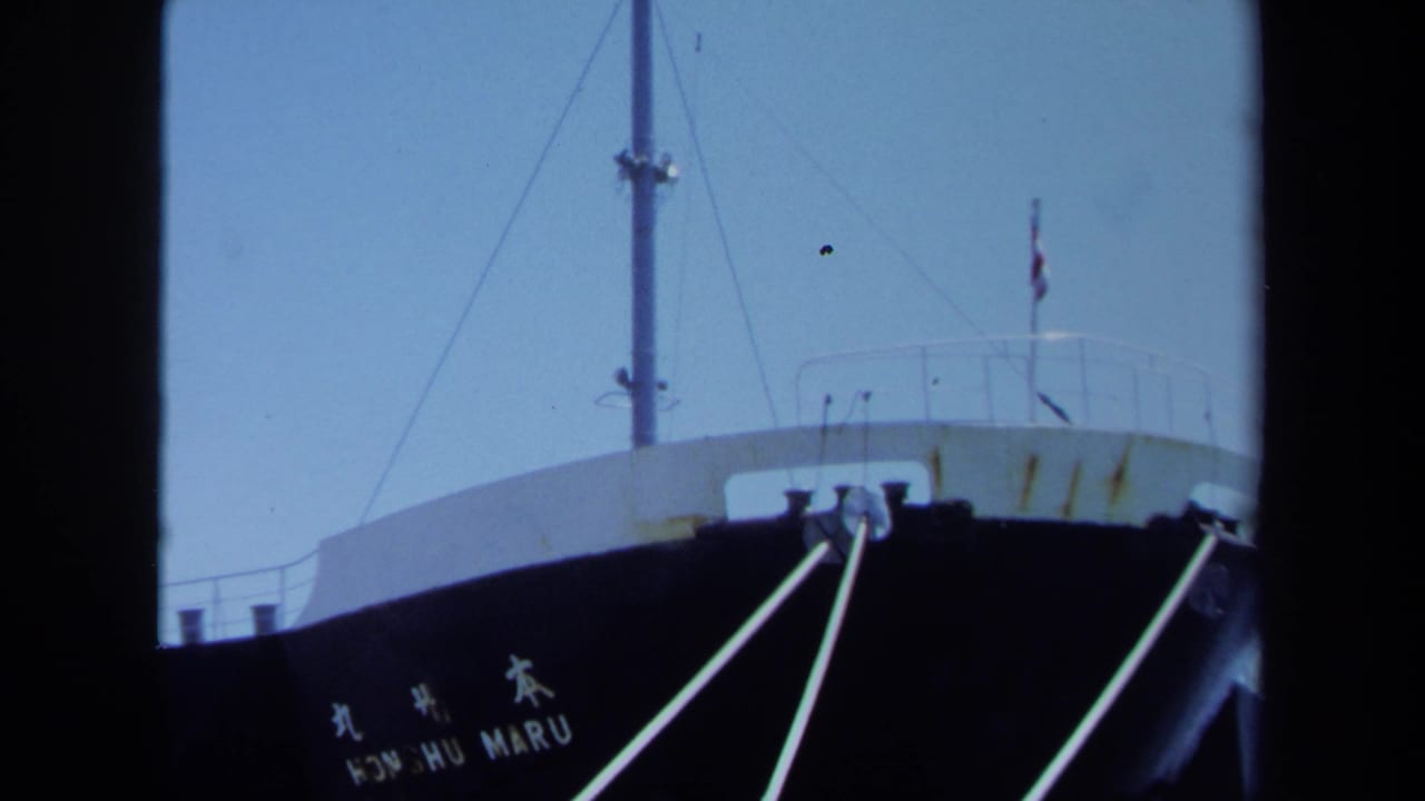 1971 Maine dockside frame showing the Honshu Maru name on a dark cargo ship hull with mooring lines and pale sky.