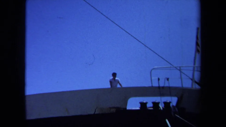 1971 Maine home-movie view of a man on a ship deck, with railings, linework, and bright blue sky behind him.