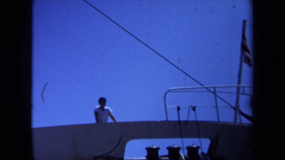 1971 Maine waterfront frame with a closer distant view of a man on deck, railings, cables, and ship fittings visible below.