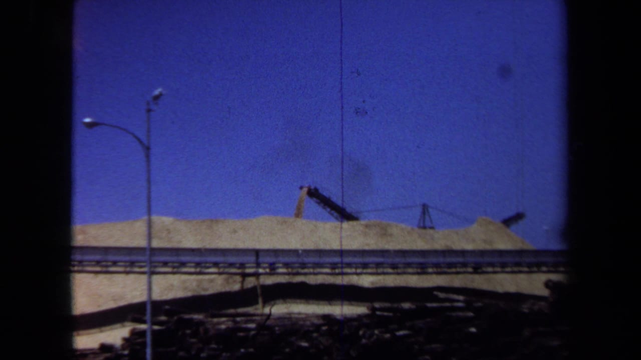 A brief partial 8mm frame shows sandy ground, a raised rail or roadway, streetlights, and dark gate edges before the park sequence.