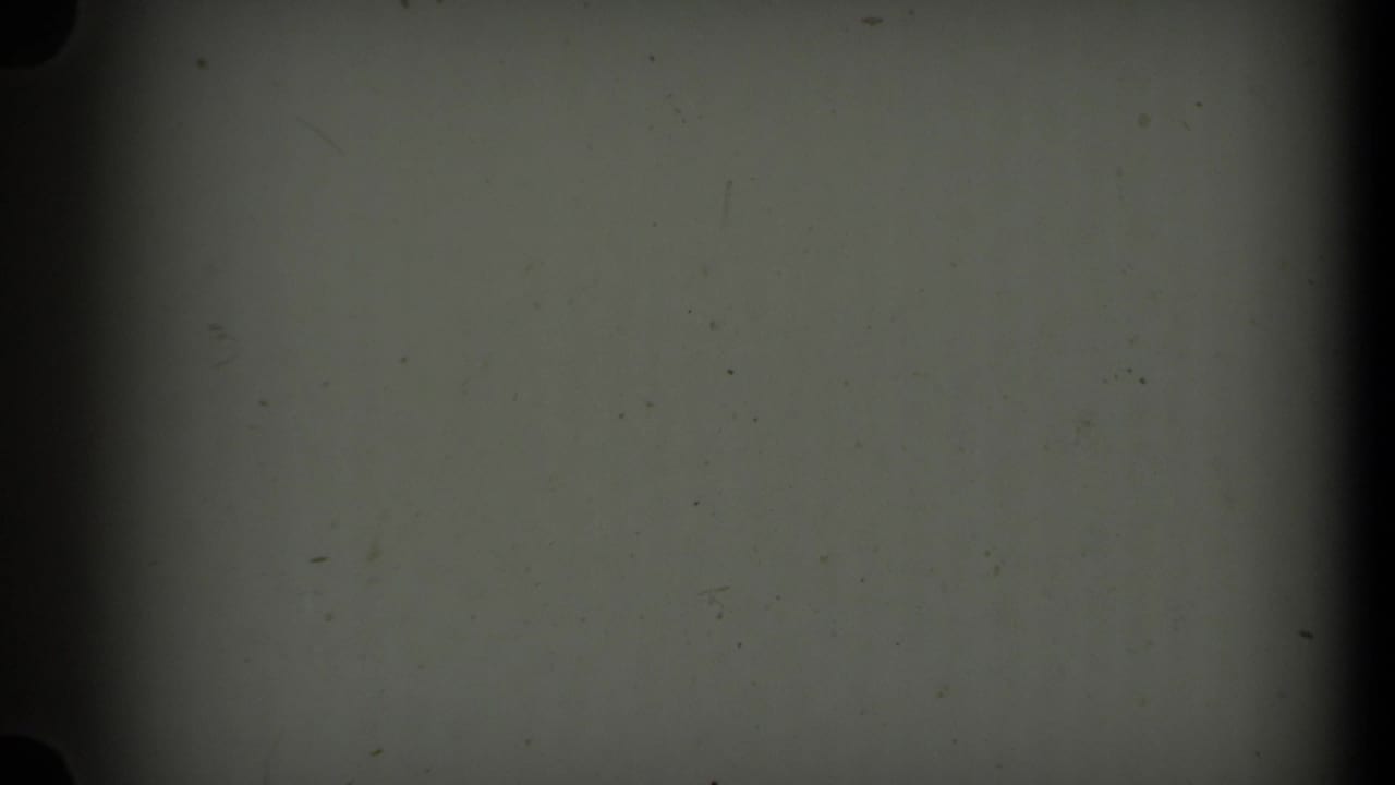 A mostly blank 8mm frame shows gray-green exposure, dust specks, and dark film-gate edges, with no clear subject visible.