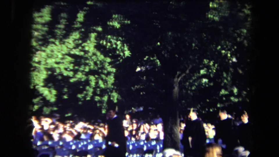 1971 Sacramento night-event footage showing participants moving near seated spectators under bright tree-filtered light.