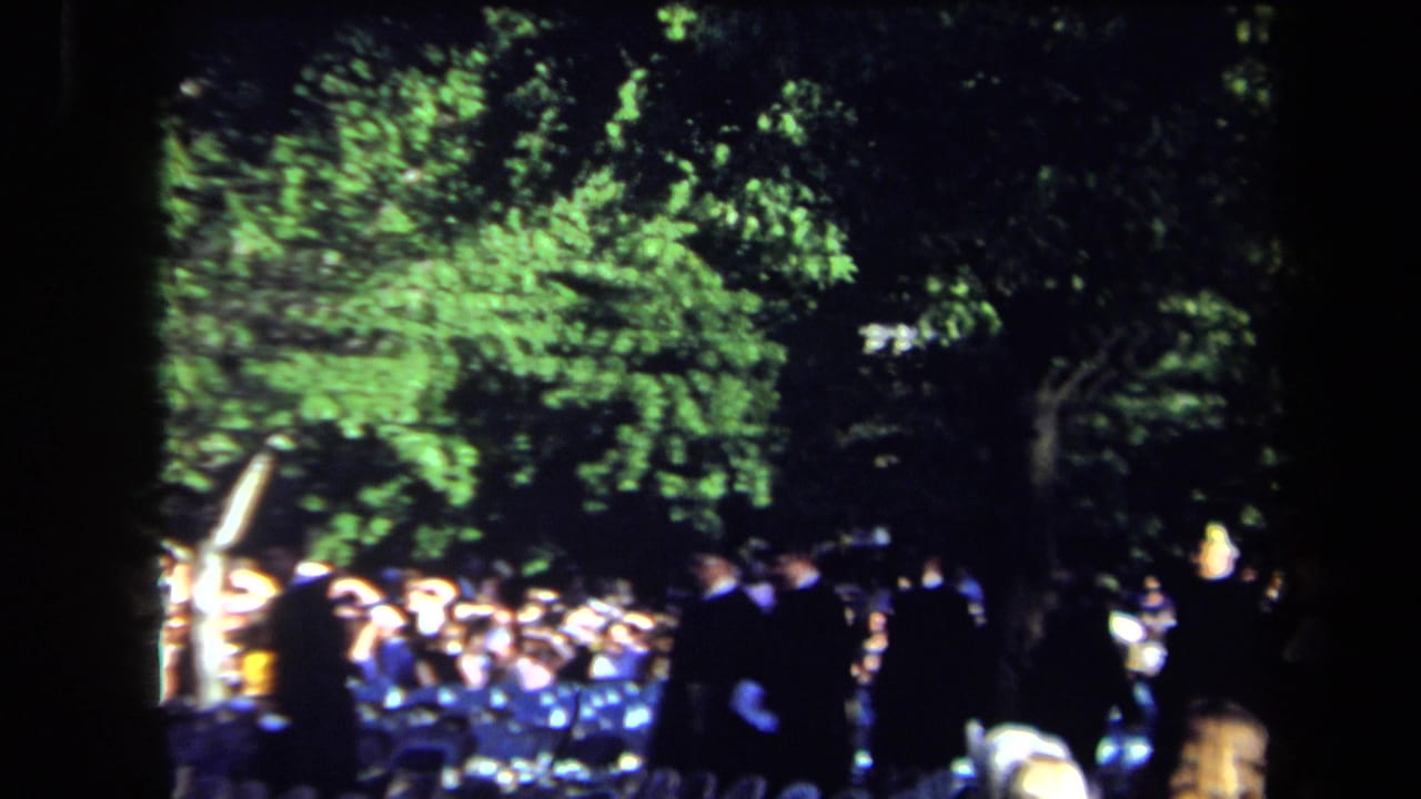 1971 Sacramento graduation crowd outdoors, with dark academic gowns, seated guests and leafy trees in bright sun.
