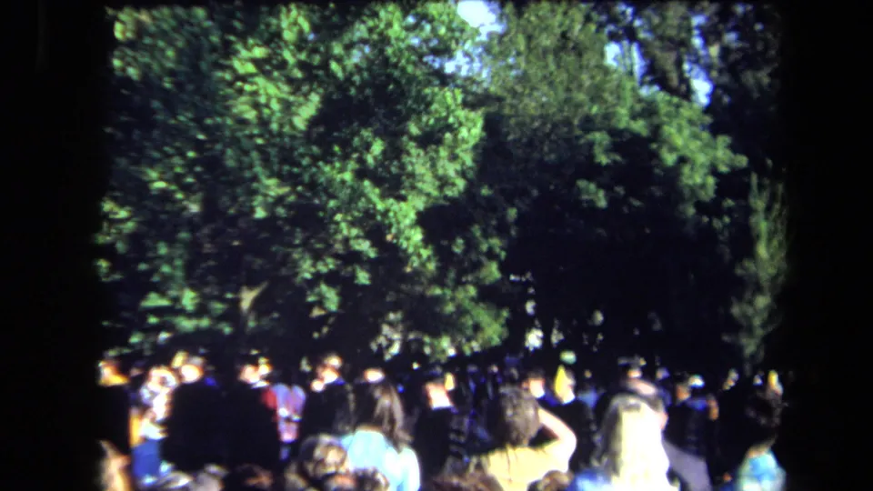 Sacramento 1971 graduation attendees stand and sit under trees, with dark academic robes visible among the crowd.