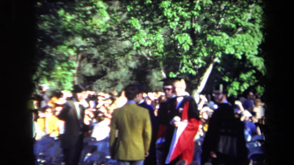 Outdoor 1971 Sacramento graduation crowd with caps, gowns, spectators, trees, and a red academic robe visible in sunlight.