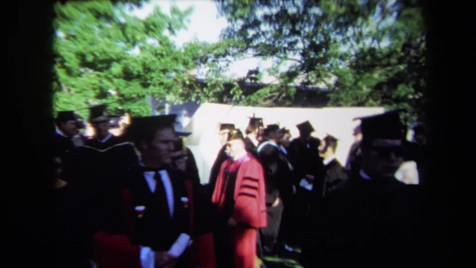 1971 Sacramento outdoor graduation scene with robed figures, mortarboards, spectators, trees, and bright afternoon exposure.