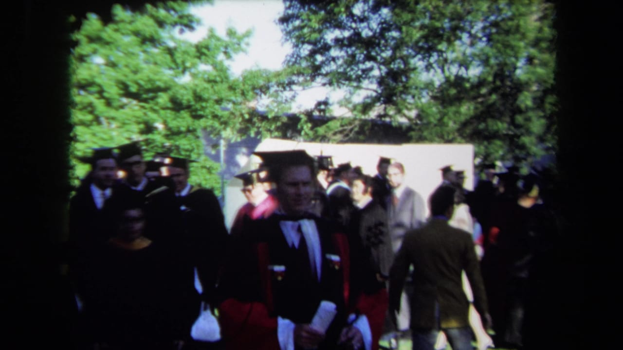 1971 Sacramento home-movie frame showing academic procession members and suited spectators at an outdoor convocation.
