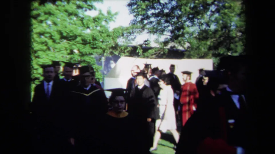 Graduates and faculty in black and red academic robes walk past spectators during the Sacramento convocation.