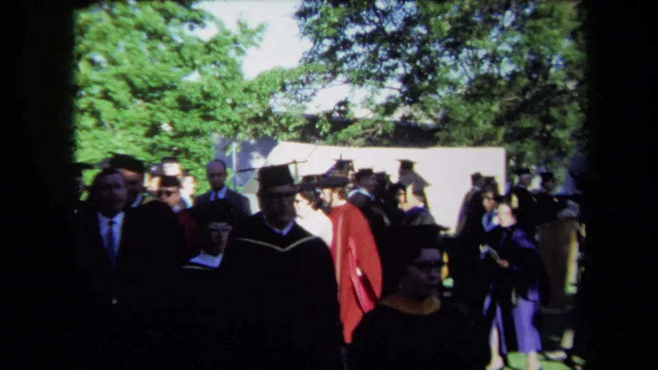 Close home-movie view of graduates and faculty in academic dress at the 1971 Sacramento outdoor ceremony.