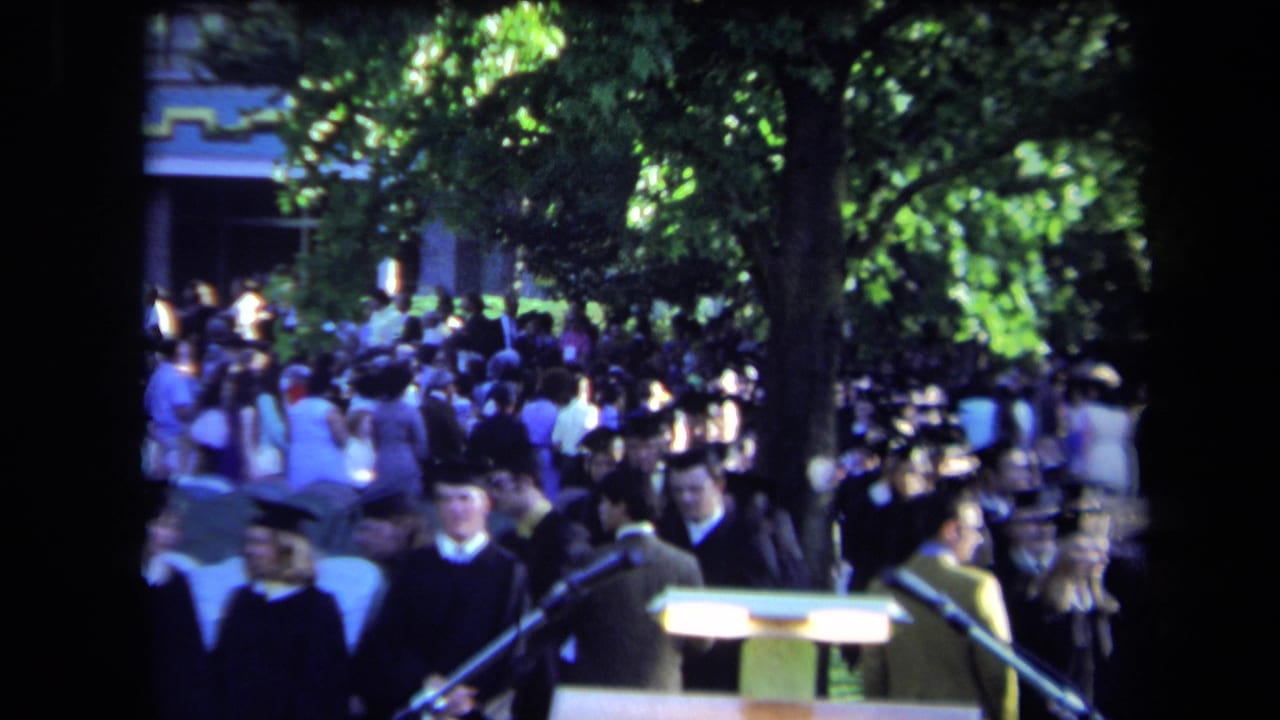 Outdoor 1971 Sacramento commencement view with graduates in mortarboards, a crowd, and ceremony microphones beneath trees.