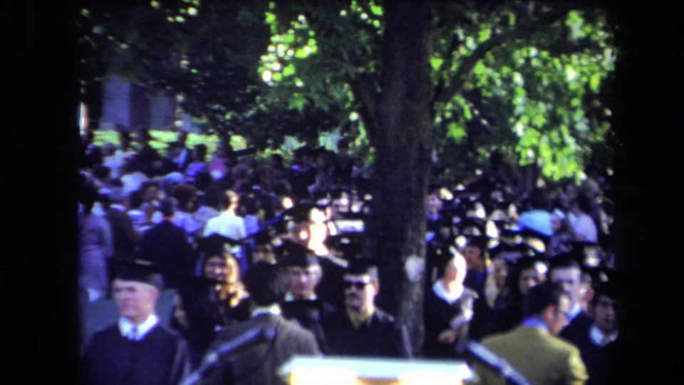 1971 Sacramento outdoor graduation crowd with faces visible, robed graduates, a large tree, and ceremony equipment in front.