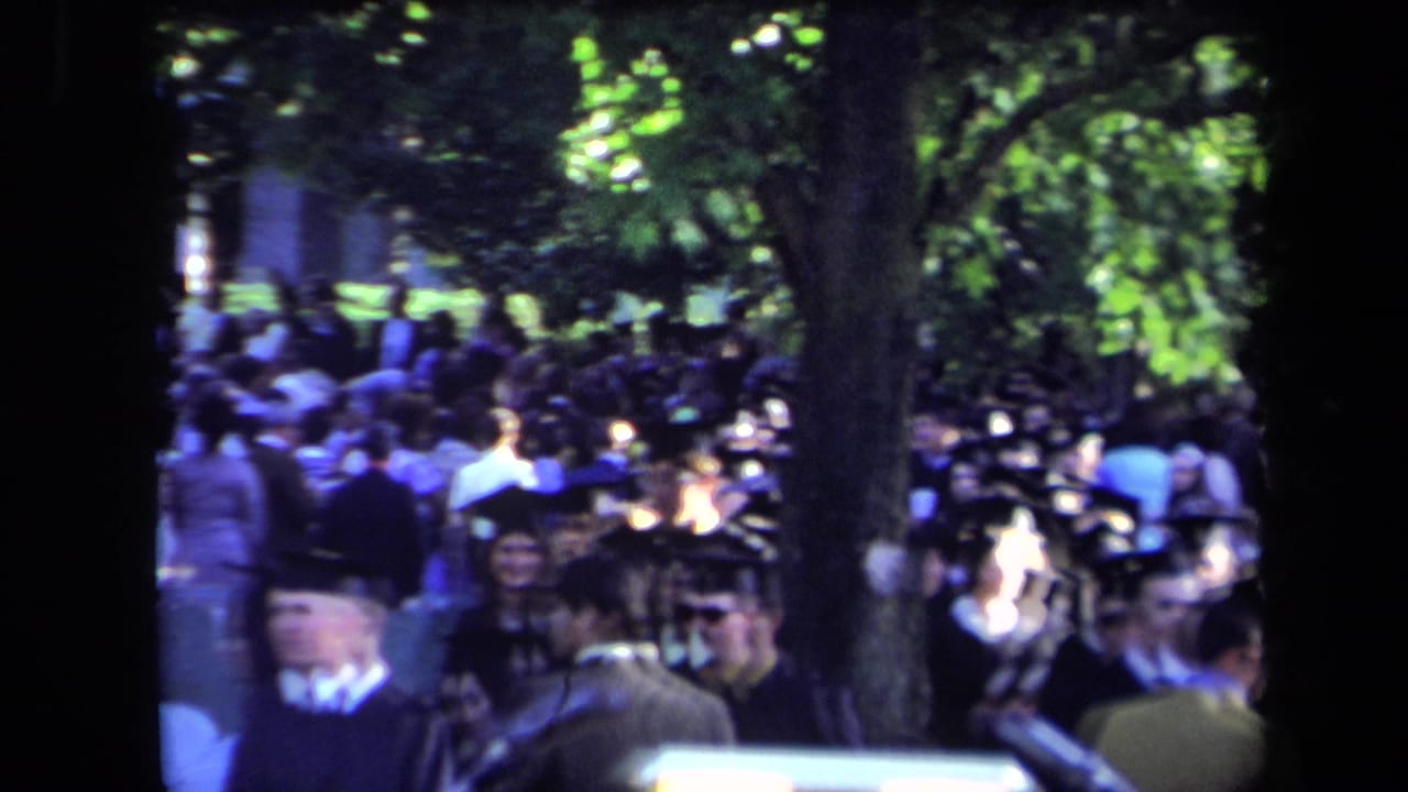 Sacramento 1971 home-movie view of graduates and attendees gathered outdoors beneath trees during a commencement ceremony.
