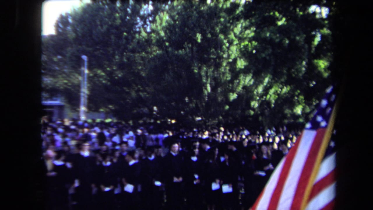A 1971 Sacramento graduation view looks across graduates in black robes with a large American flag at the edge of the frame.