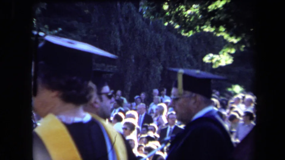 Outdoor Sacramento graduation scene with academic caps, gowns, yellow stole, and a crowded audience in the background.