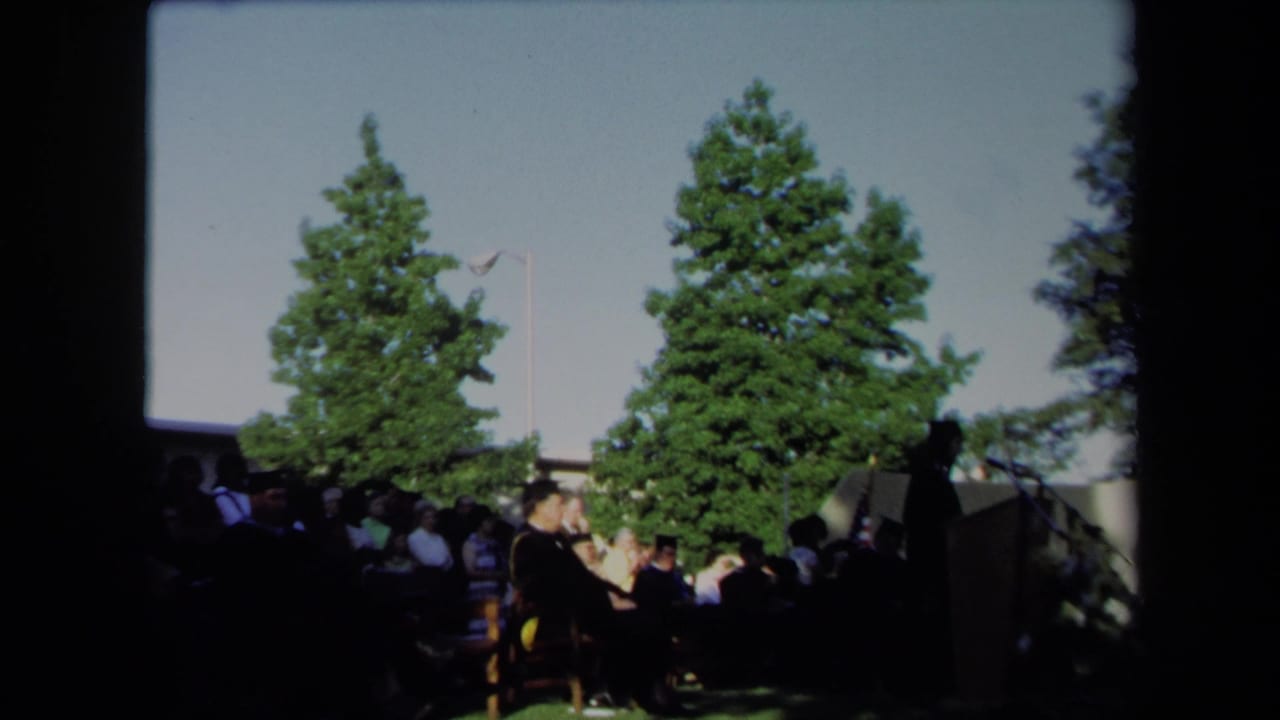 1971 Sacramento outdoor graduation scene with seated graduates or faculty near a podium under tall trees.