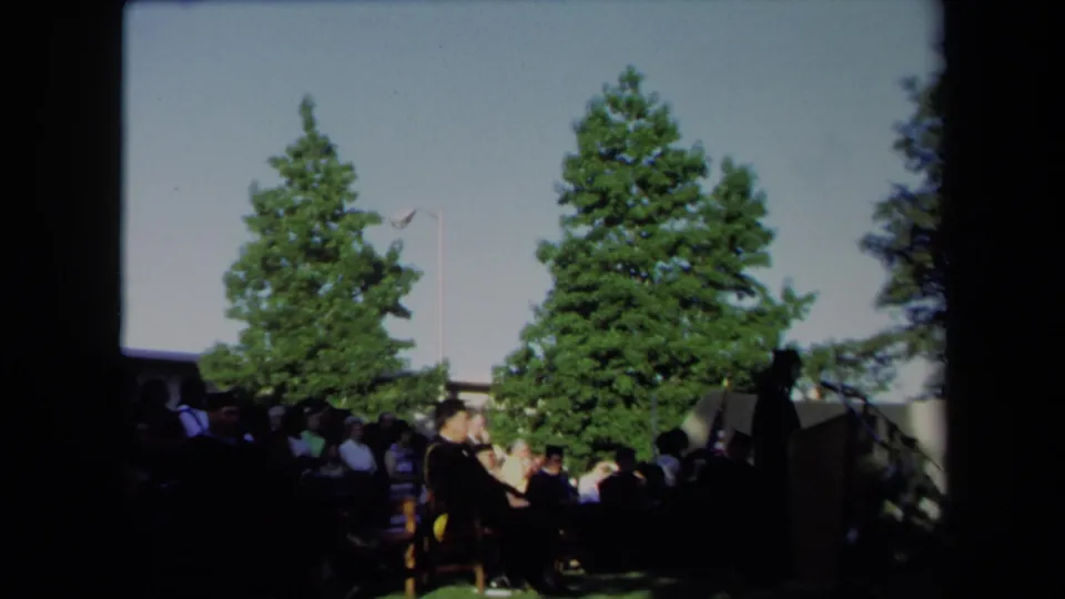 1971 Sacramento outdoor graduation scene with seated graduates or faculty near a podium under tall trees.
