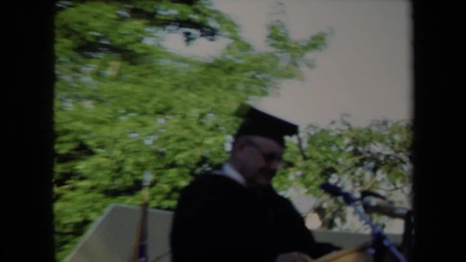 Close home-movie view of a person in cap and gown passing the camera at the 1971 Sacramento graduation.