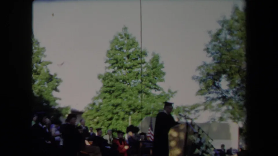 The outdoor 1971 Sacramento commencement scene shows a speaker at the podium with graduates seated behind him under tall trees.