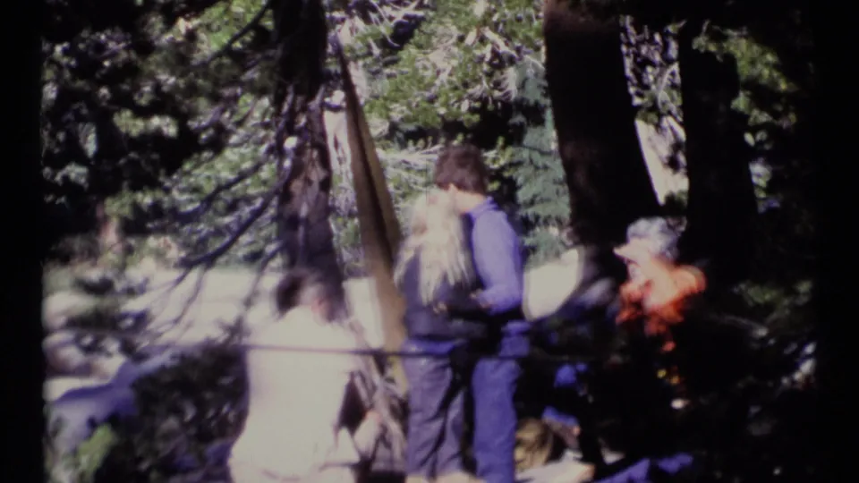 1973 Scapegoat Wilderness home-movie frame showing adults among conifers, including a couple standing close together.