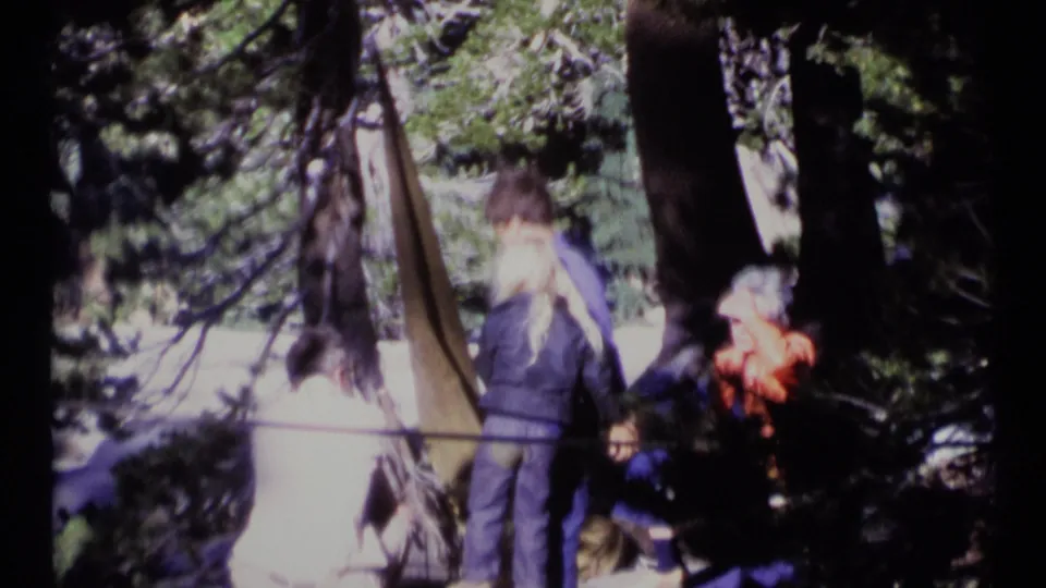 1973 8mm frame of the couple moving slightly in the Scapegoat Wilderness trees while companions remain nearby.