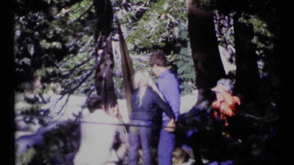 The final frame shows the couple embracing in a shaded Montana forest, with a seated companion in orange clothing nearby.